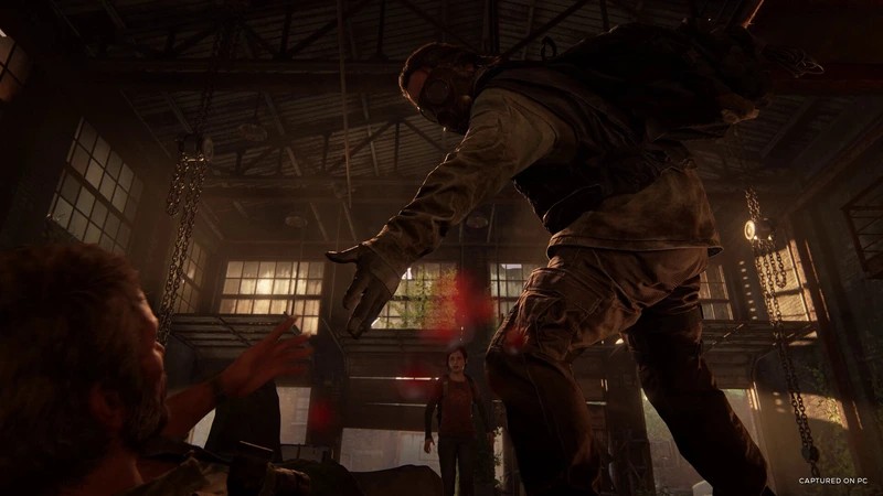 A masked attacker looms over Joel inside an industrial building in The Last of Us Part I