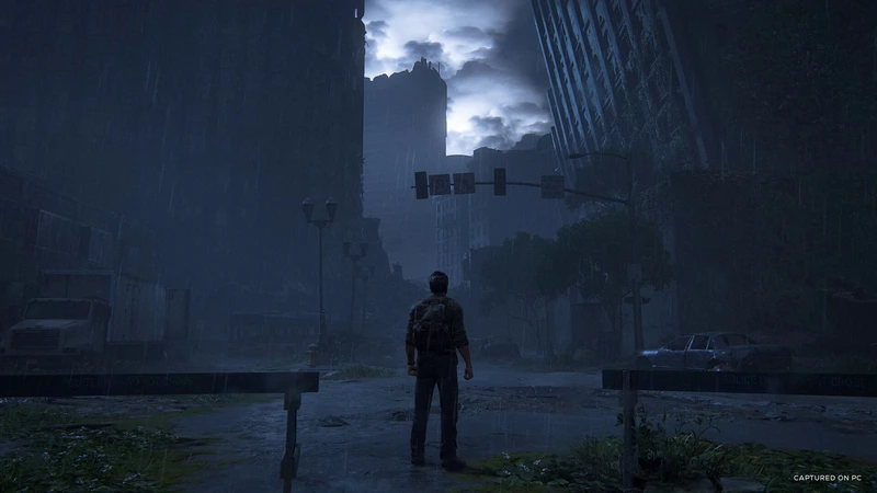 Joel stands on a rain-soaked city street in The Last of Us Part I