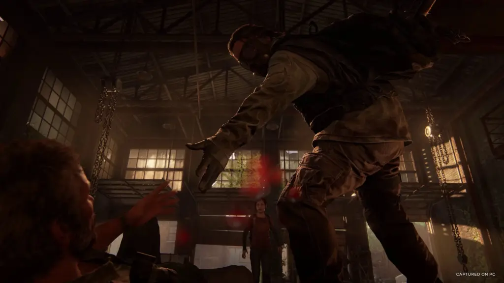 A masked attacker looms over Joel inside an industrial building in The Last of Us Part I